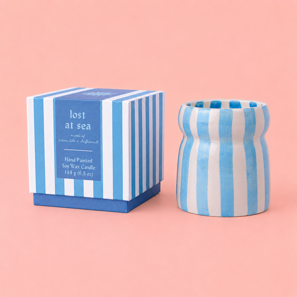 Lost at Sea candle in a blue and cream striped ceramic vessel beside its matching striped gift box.