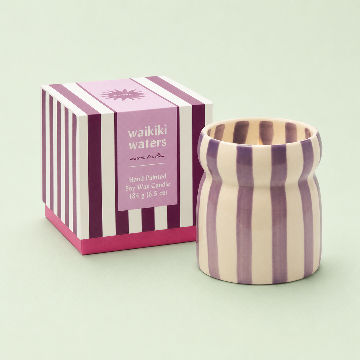 Waikiki Waters soy wax candle in a purple and cream striped ceramic vessel beside its matching striped box.