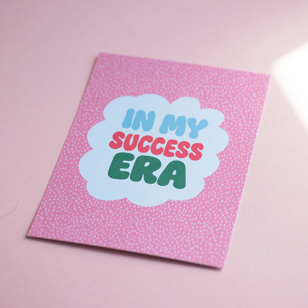 Cheerful In My Success Era A5 print with colourful retro lettering and a white scalloped centre on a pink patterned background.