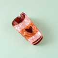 Coffee cup hair claw clip in pearlescent pink and caramel tones with a dark heart detail on a pale mint background.