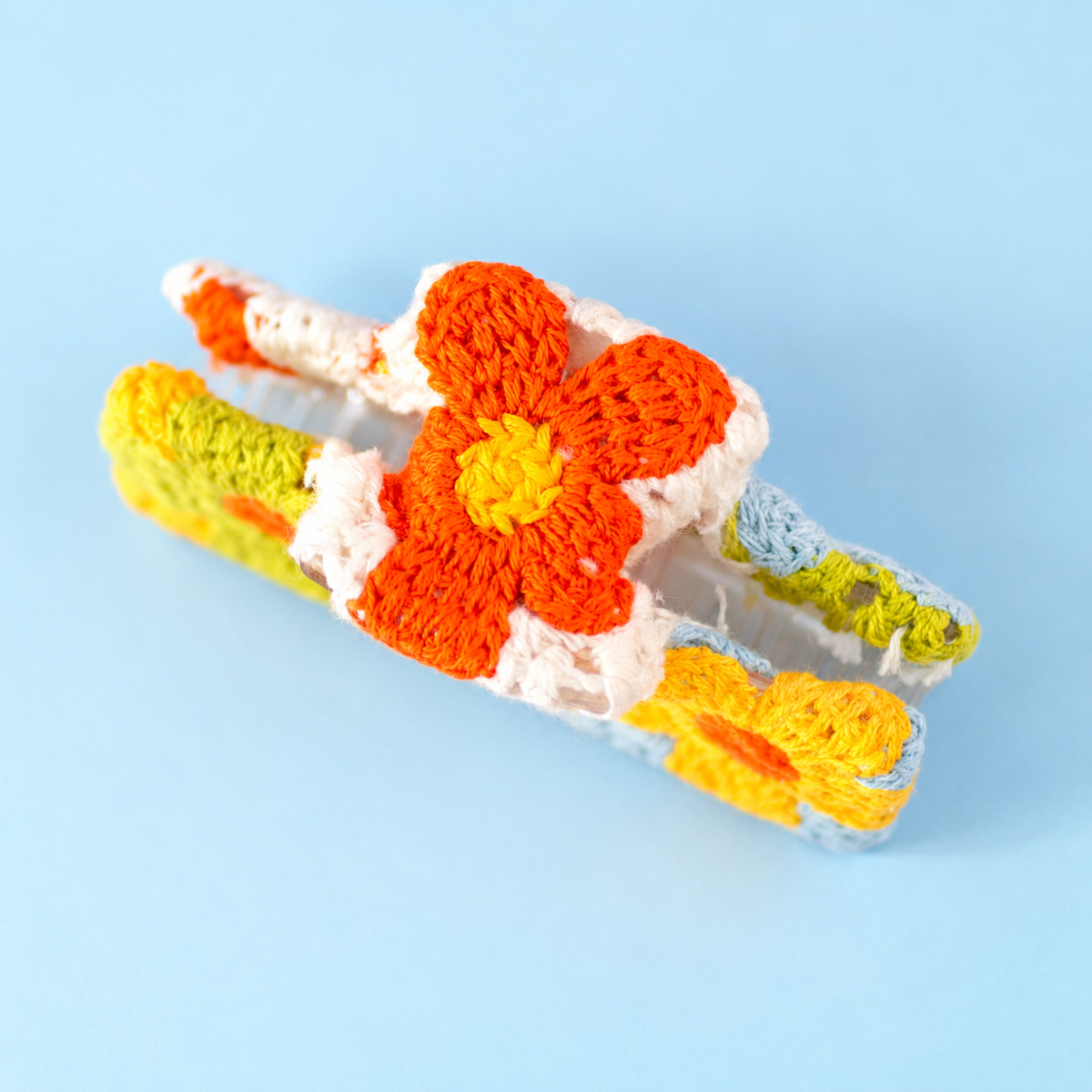 Close up of colourful crochet flower claw clip showing orange flower detail on a pale blue background.