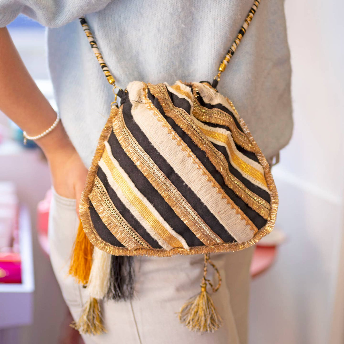Black and gold tassel handbag styled crossbody, bringing a fabulous touch of boho texture and shimmer to a neutral outfit.