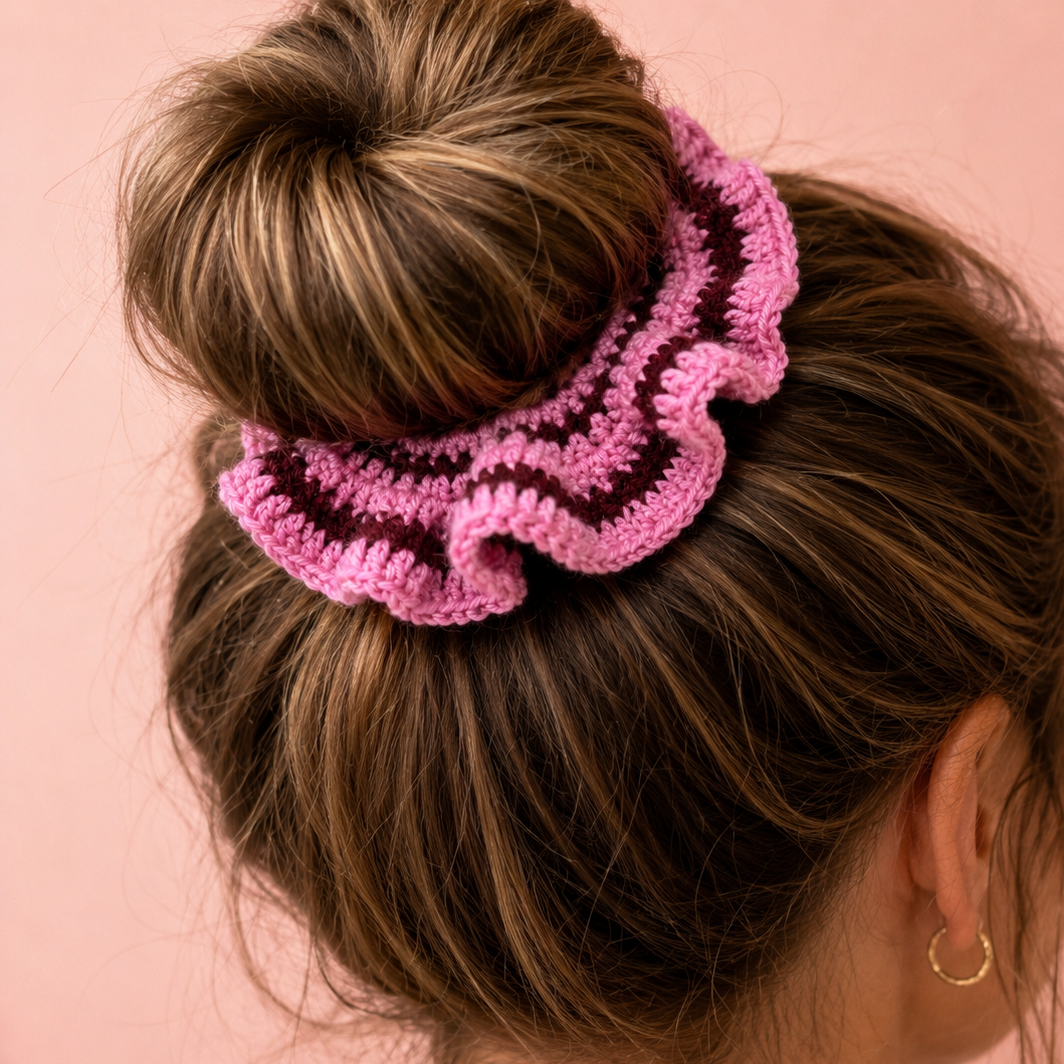 Raspberry Ruffle handmade crochet scrunchie in pink and deep berry tones worn around a brunette bun.