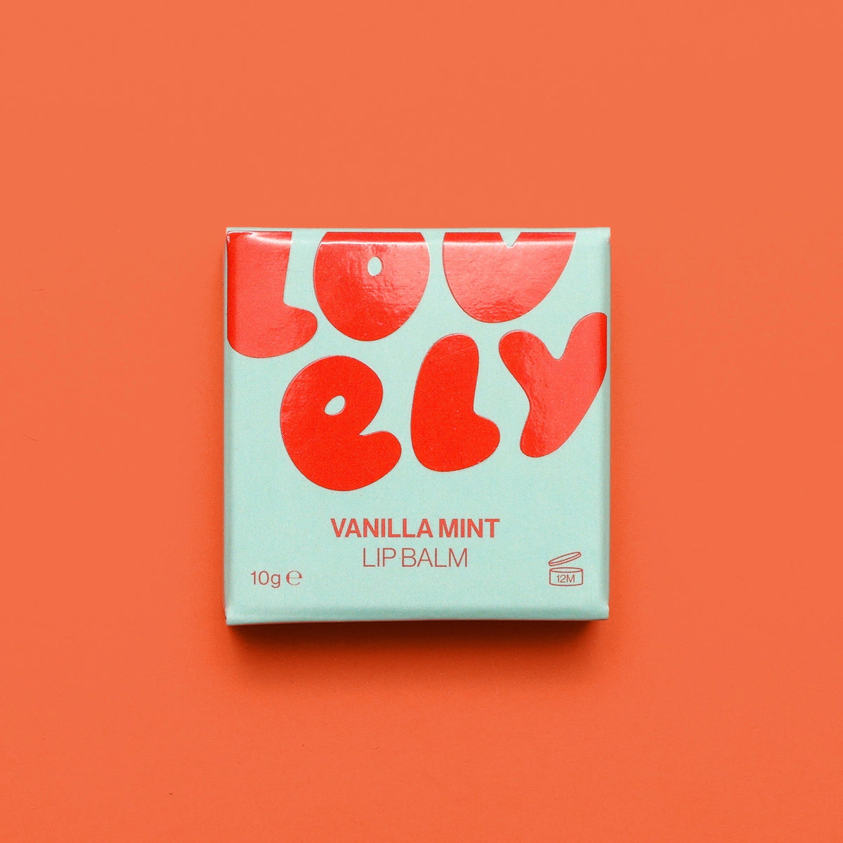 Vanilla Mint Lip Balm in pale blue and red packaging photographed against a bright orange background.
