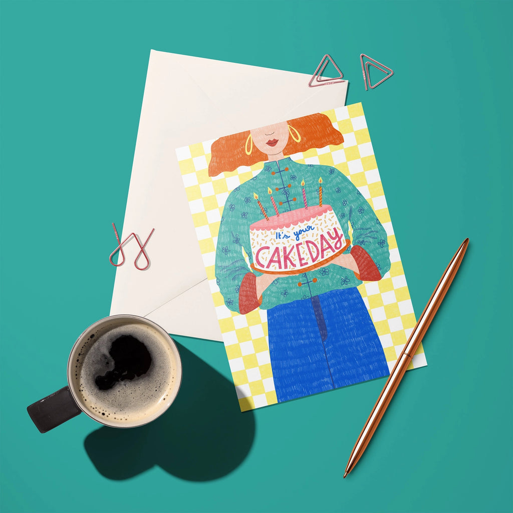 Colourful It’s Your Cake Day birthday card with illustrated cake, candles and yellow checked background styled with envelope and coffee.
