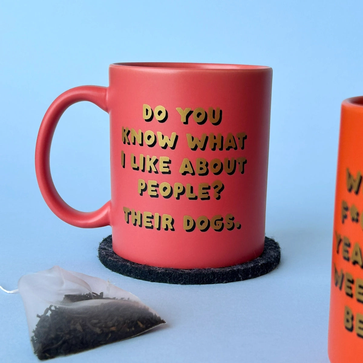 Pink ceramic dog lover mug on a dark coaster with a tea bag in front against a pale blue background.