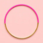 Vibrant pink dip enamel stacking bangle with polished gold tone detailing on a pale pink background.