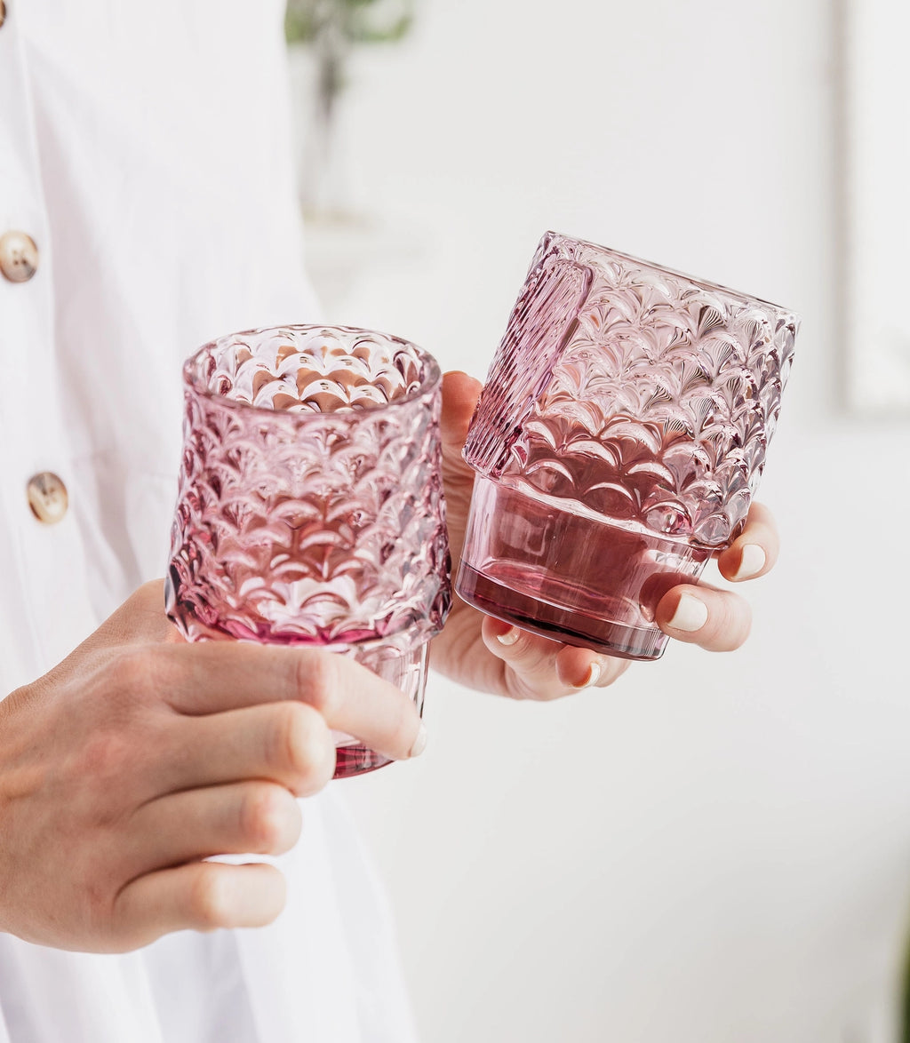 Two pink textured fish drinking glasses held in hands showing their different shapes.