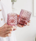 Two pink textured fish drinking glasses held in hands showing their different shapes.