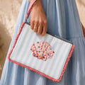 Joyful blue and white striped clutch with a sparkling pink shell motif and colourful coral trim, carried by its wrist strap.