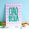 Bright Ciao Bella A5 print with green lettering and a pink harlequin pattern, styled in a cheerful kitchen setting.
