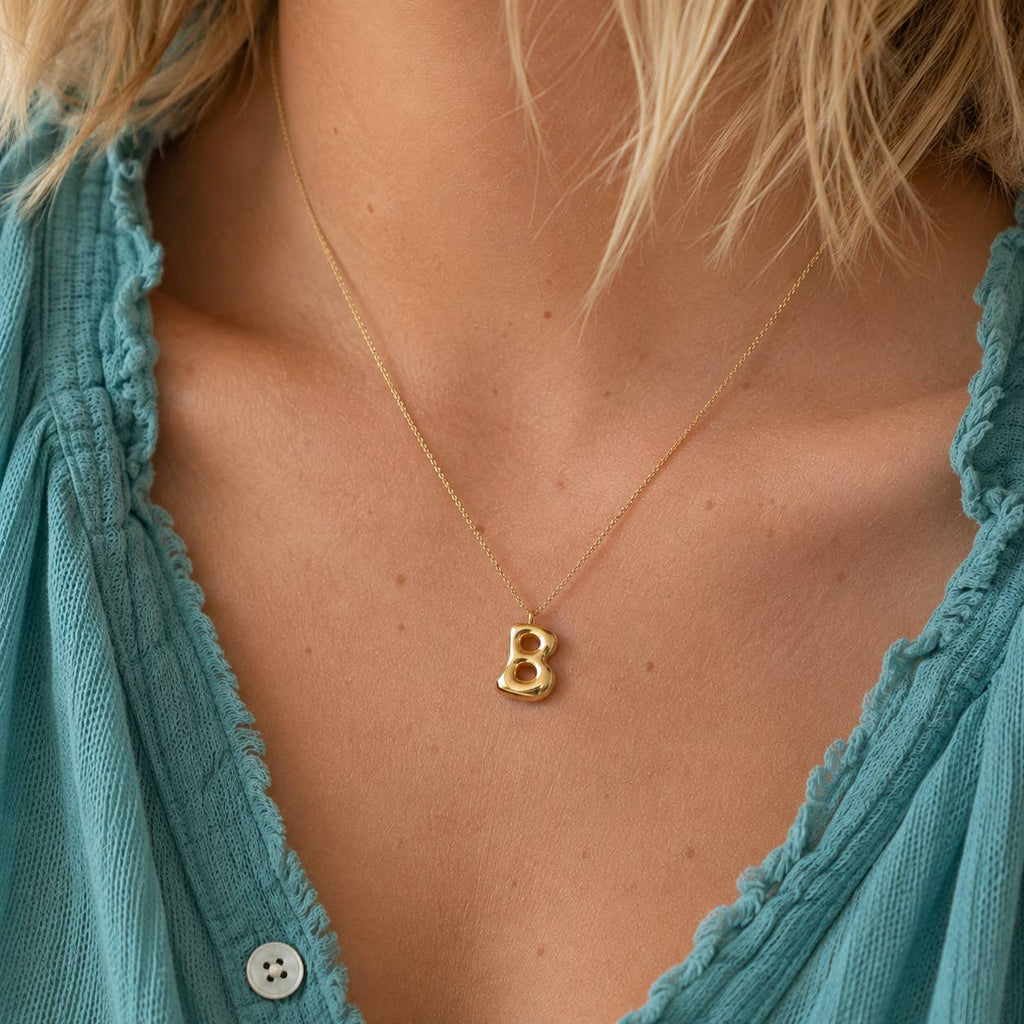 Gold bubble B initial necklace on a delicate chain, styled with a blue top for an everyday personalised jewellery look.