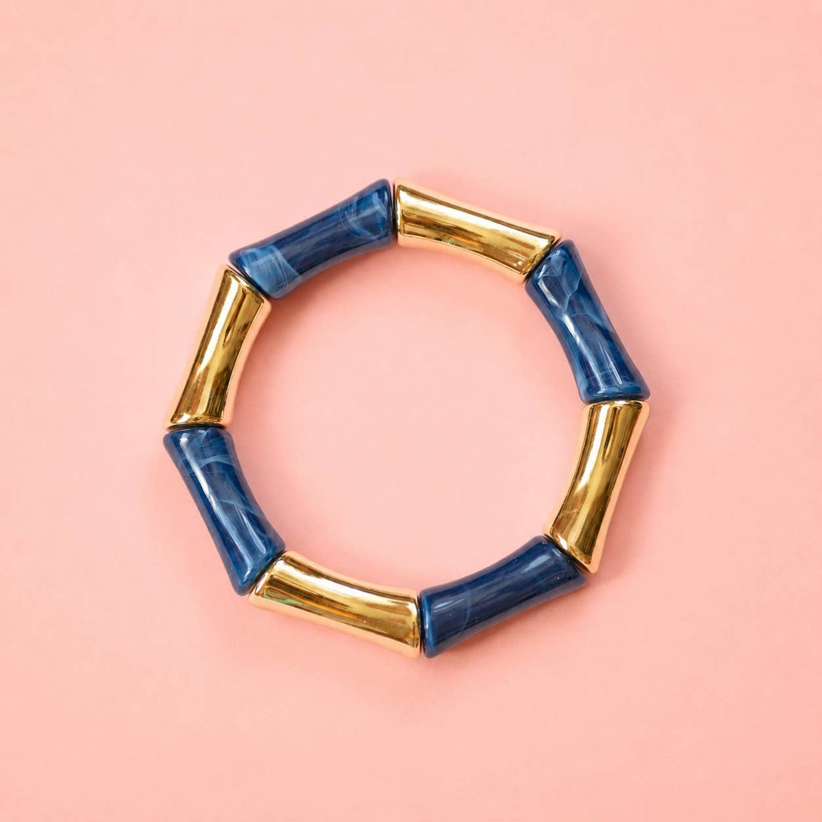 Navy marbled acrylic and gold bamboo inspired stretch bracelet on a pale pink background.