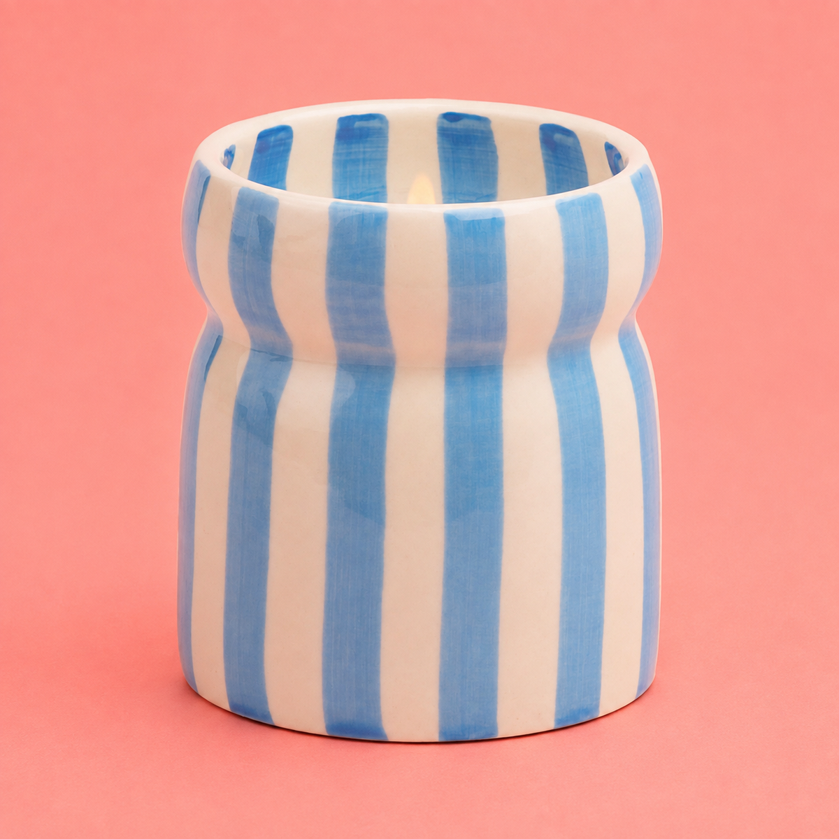 Hand painted blue and cream striped Lost at Sea ceramic candle with a softly glowing flame.