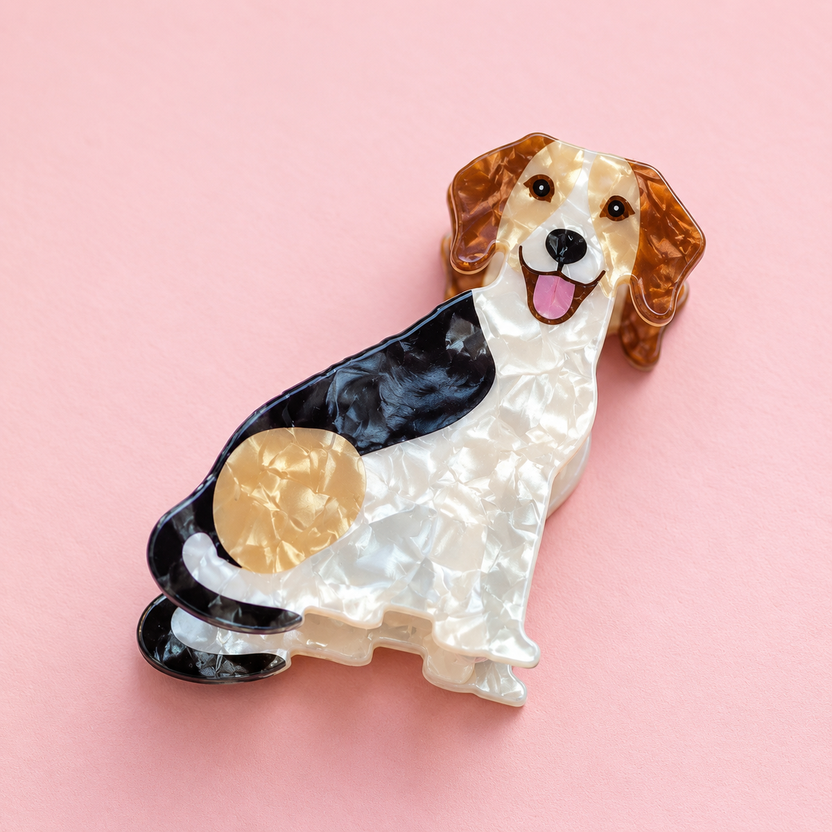 Dog shaped acrylic claw hair clip in pearlescent cream, caramel and black with floppy ears and a happy face on a soft pink background.