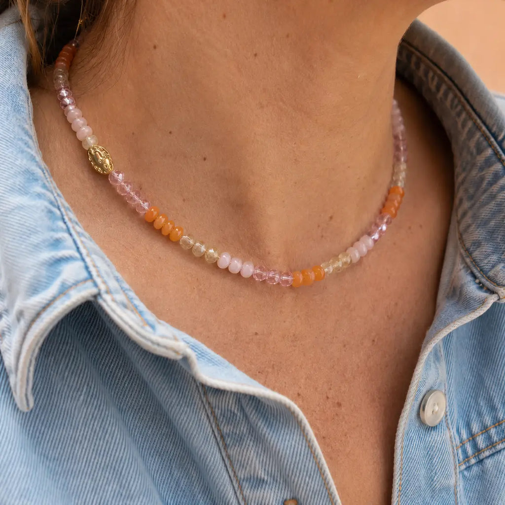 Sunrise natural stone bead necklace with peach, blush pink, honey and crystal accent beads worn with a denim shirt.
