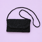 Black beaded shoulder and clutch bag with long beaded strap displayed on a pale lilac background.