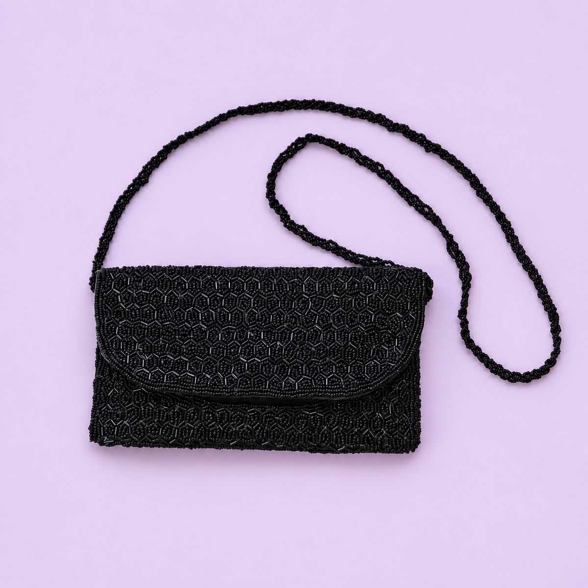 Black beaded shoulder and clutch bag with long beaded strap displayed on a pale lilac background.