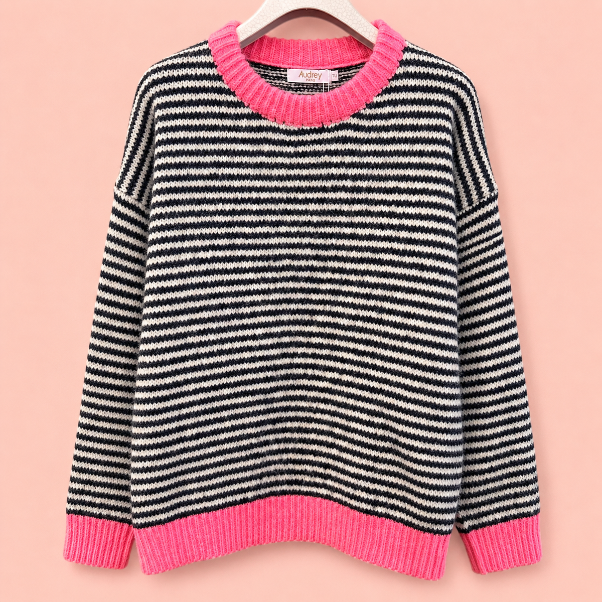 Black and white striped knitted jumper with bright pink neckline, cuffs and hem against a soft pink background.