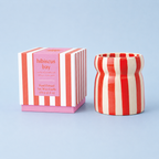 Hibiscus Bay soy wax candle beside its pink and red striped presentation box on a pale blue background.