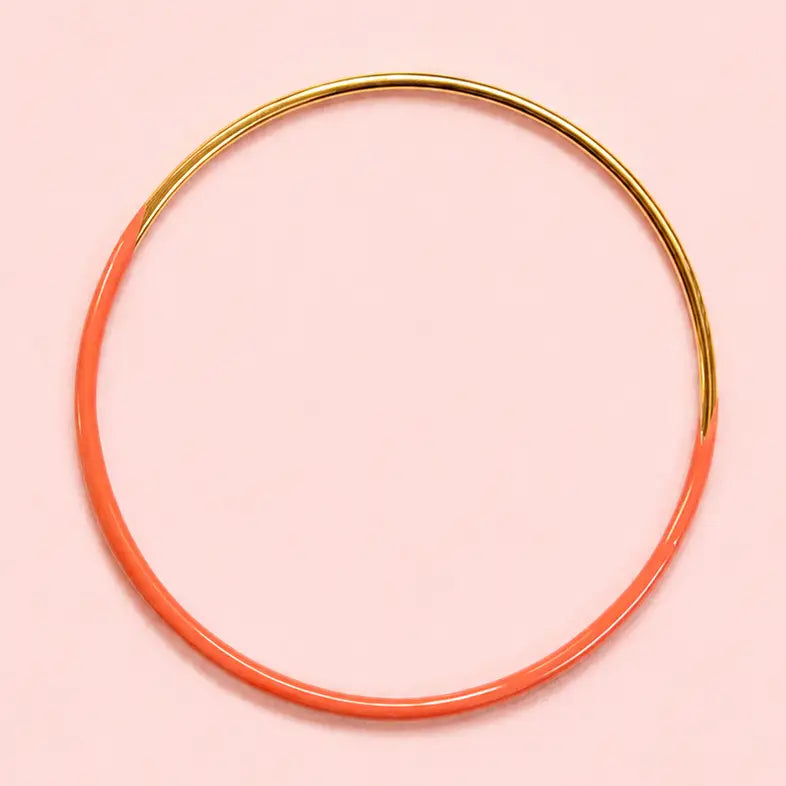Orange dip enamel stacking bangle with polished gold tone detailing on a pale pink background.