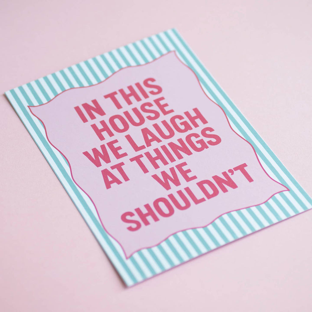Colourful In This House We Laugh At Things We Shouldn’t A5 art print in bright pink and mint, displayed on a soft pink background.