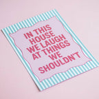 Colourful In This House We Laugh At Things We Shouldn’t A5 art print in bright pink and mint, displayed on a soft pink background.