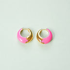 Bright pink enamel huggie hoop earrings with polished gold-tone detailing displayed on a pale green background.