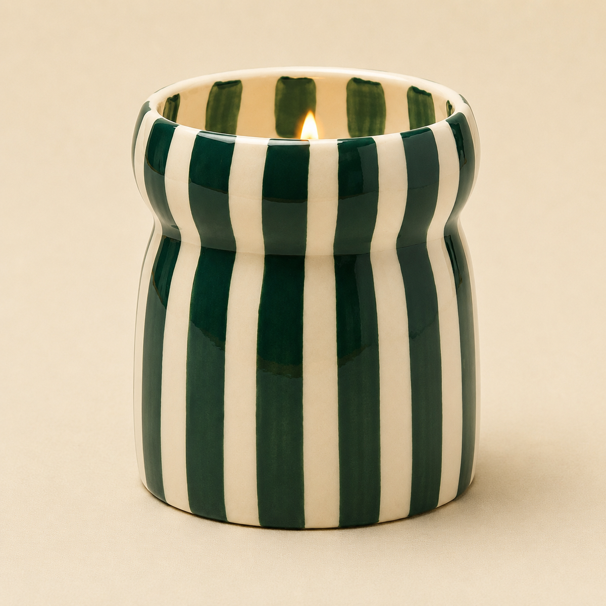 Close up of the lit Isla Fresa candle showing its hand painted green stripes and pinched ceramic shape.