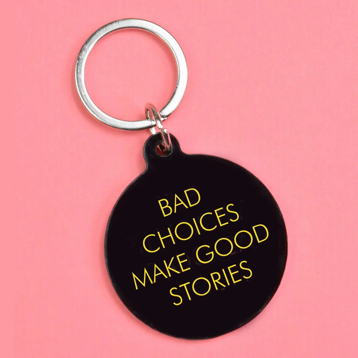 Black round keyring with yellow text reading Bad Choices Make Good Stories and a silver keyring attachment.