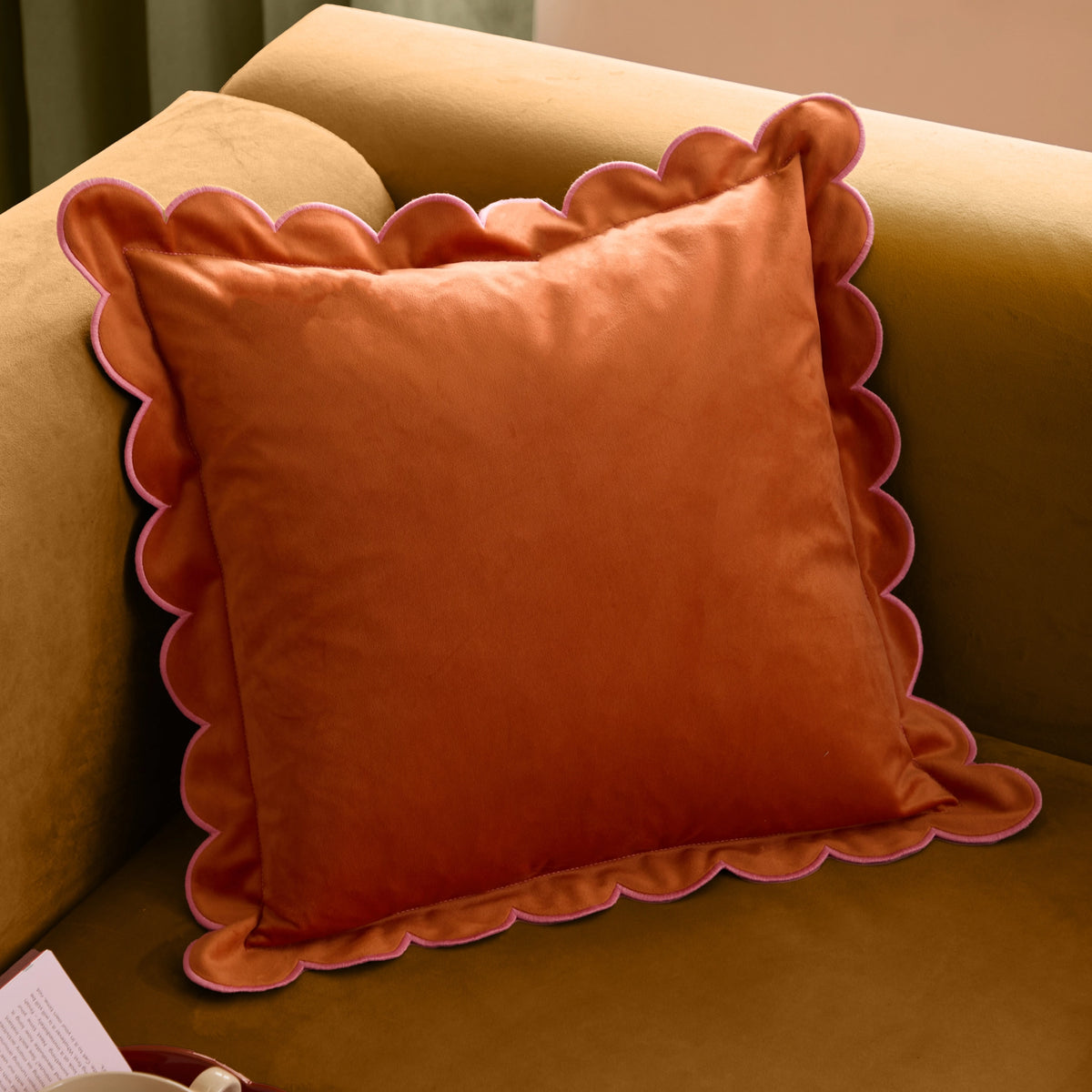 Orange velvet cushion with scalloped edging and contrasting pink trim styled on a warm brown sofa.