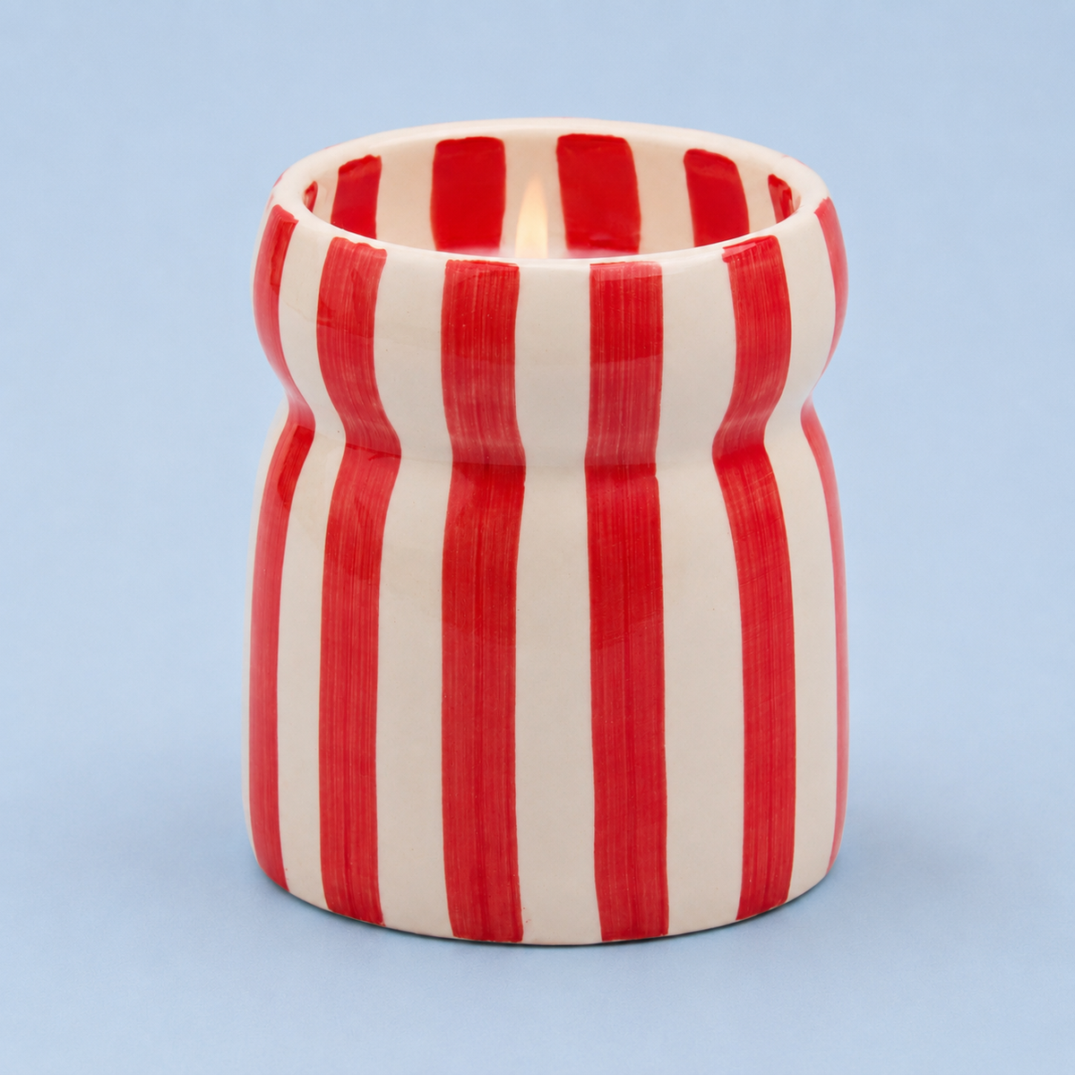 Hibiscus Bay candle in a hand painted red and cream striped ceramic vessel on a pale blue background.