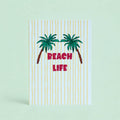 Cheerful Beach Life A5 print with two green palm trees, pink lettering and sunny yellow stripes on a pale background.