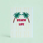 Cheerful Beach Life A5 print with two green palm trees, pink lettering and sunny yellow stripes on a pale background.