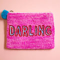 Bright pink beaded zip pouch with red and blue sequin ‘DARLING’ lettering and a blue pom pom zip pull.