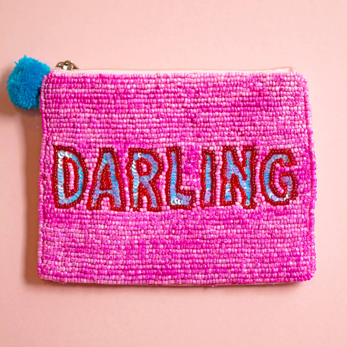 Bright pink beaded zip pouch with red and blue sequin ‘DARLING’ lettering and a blue pom pom zip pull.