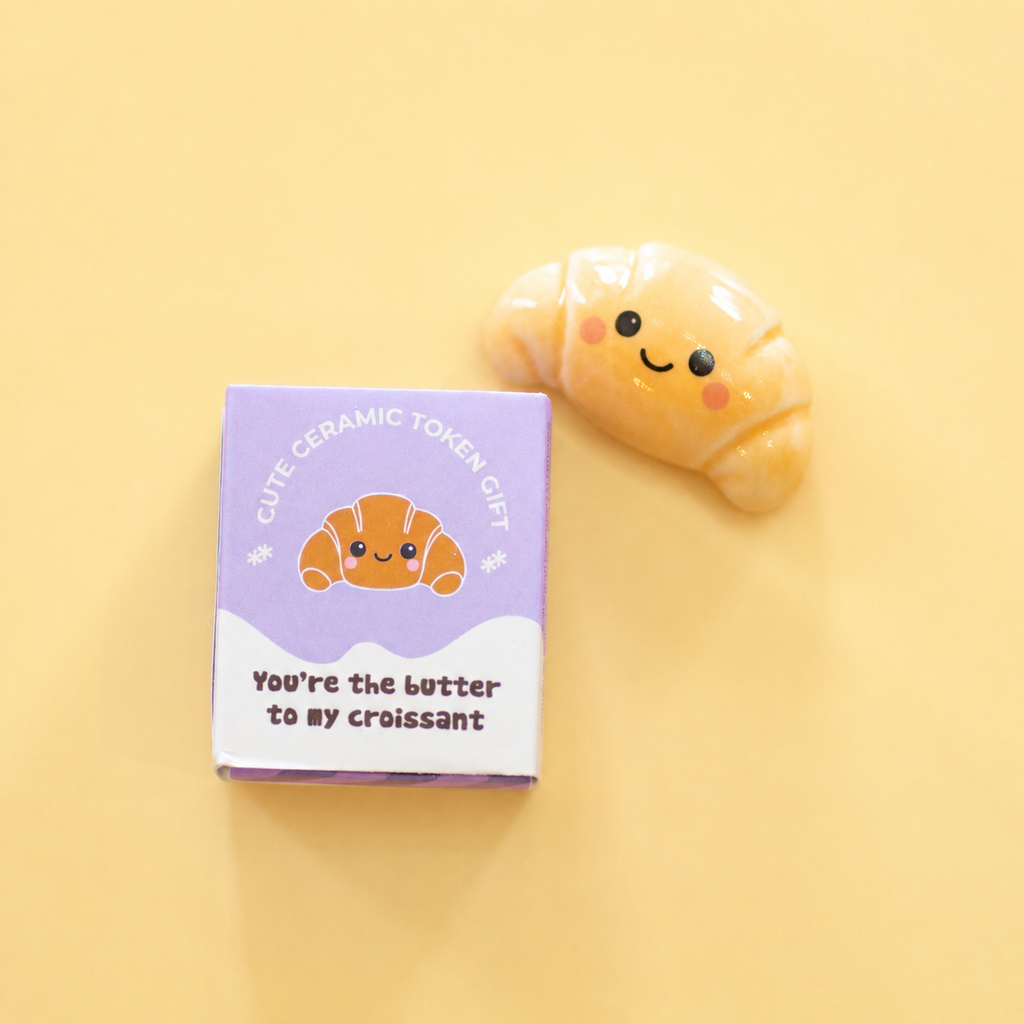 Ceramic croissant token beside its gift box reading You’re the butter to my croissant on a soft yellow background.