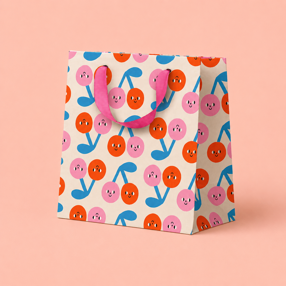 Colourful square gift bag with smiling pink and orange cherry print, blue stems and bright pink ribbon handles.