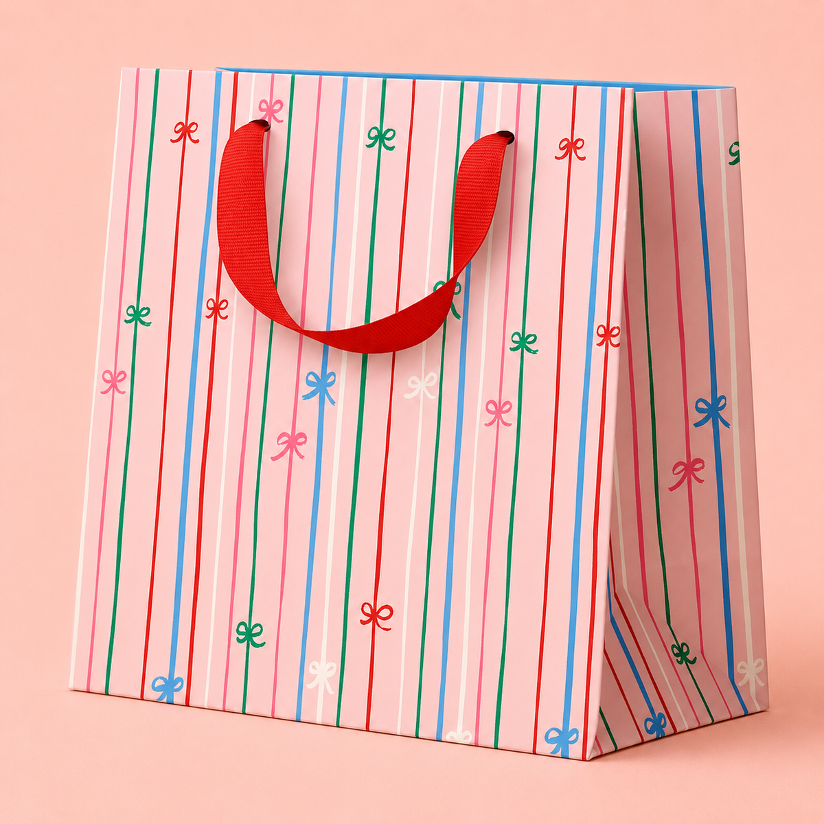 Pale pink gift bag with colourful vertical stripes, tiny bow details and a bright red ribbon handle.