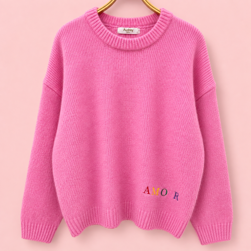 Front of pink knitted jumper with small multicoloured AMOUR embroidery near the hem.
