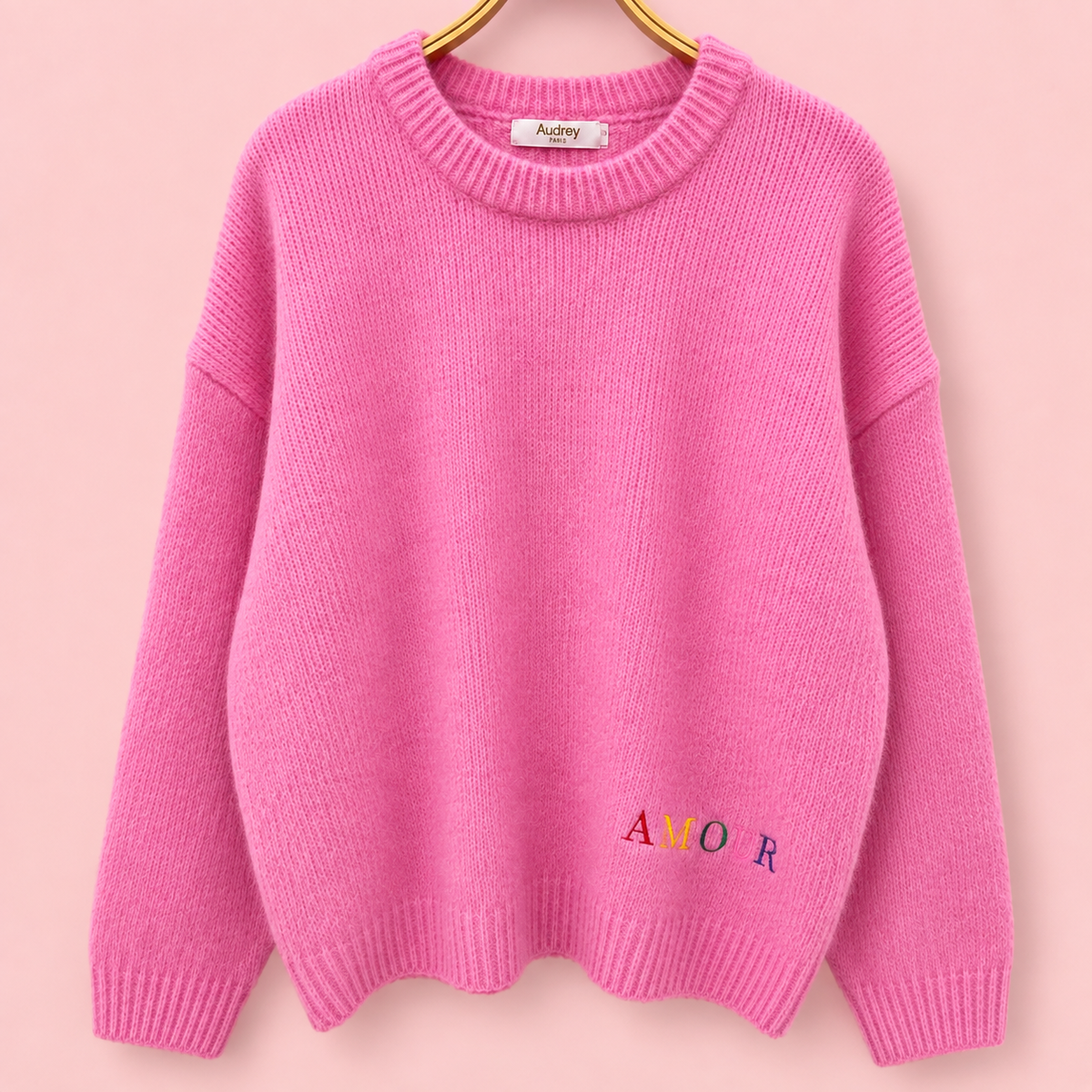 Front of pink knitted jumper with small multicoloured AMOUR embroidery near the hem.
