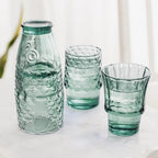 Green fish glasses partly stacked with two tumblers filled with drinks and ice.