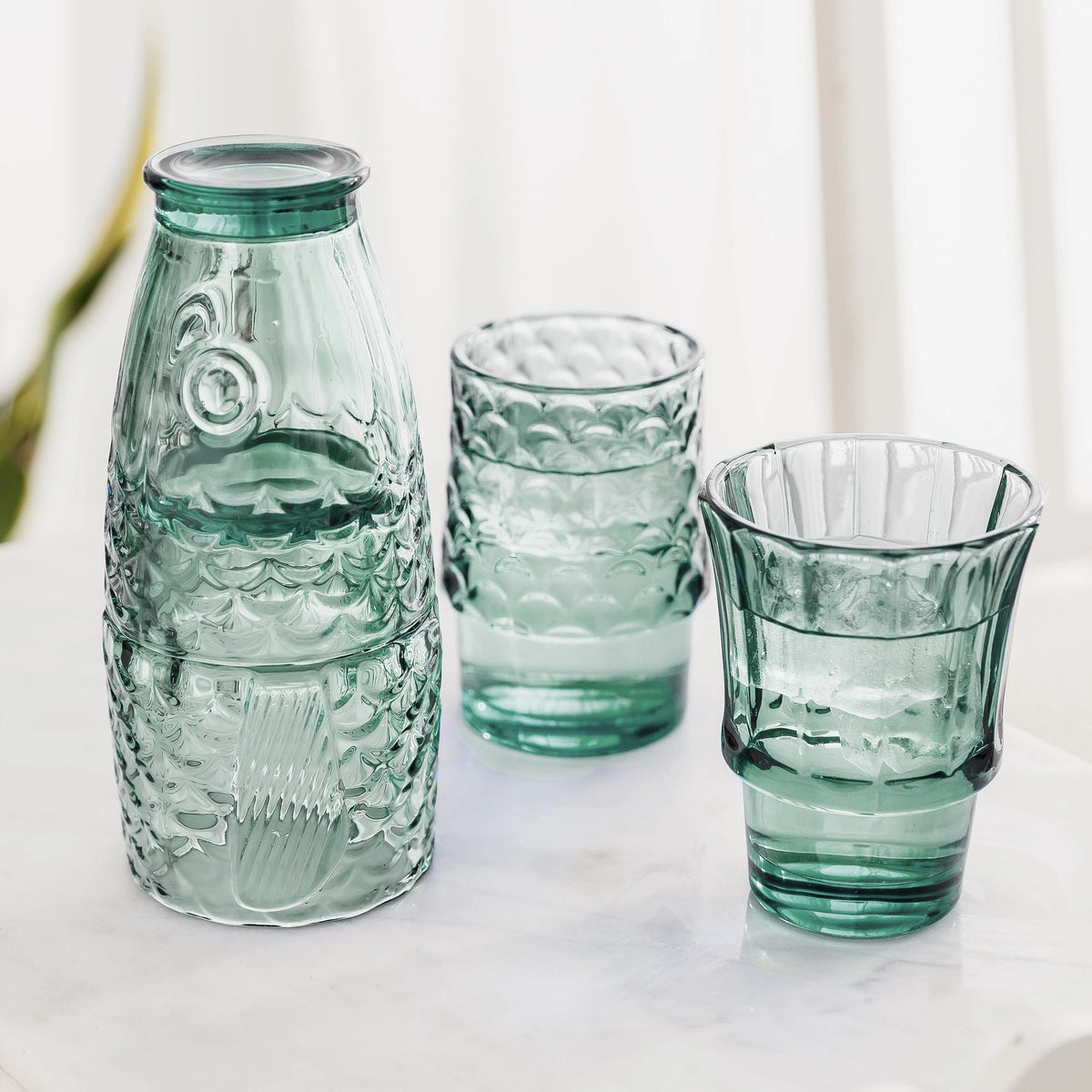 Green fish glasses partly stacked with two tumblers filled with drinks and ice.