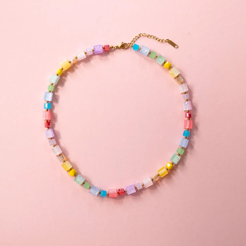 Colourful pastel crystal cube necklace arranged in a circle on a pale pink background.