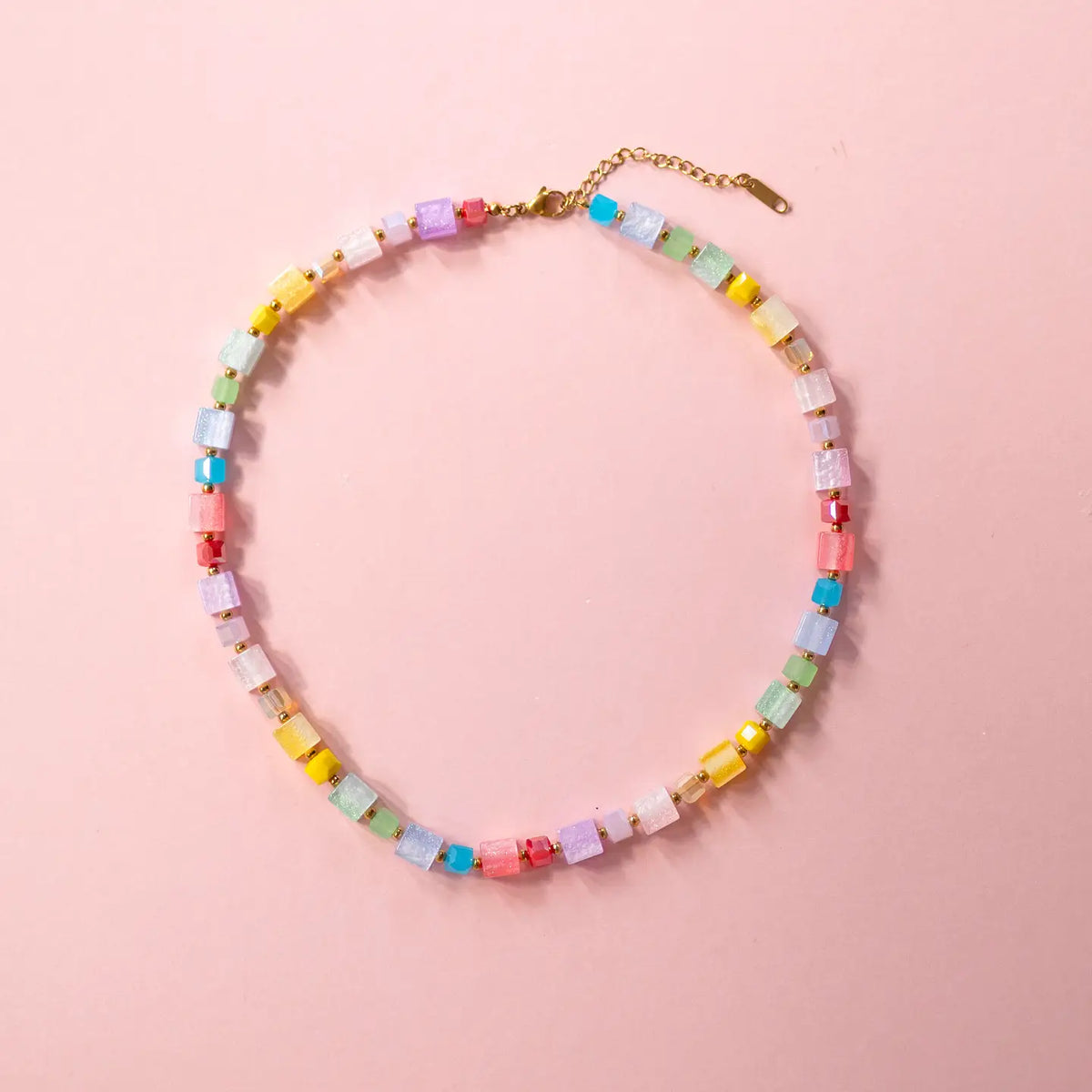 Colourful pastel crystal cube necklace arranged in a circle on a pale pink background.