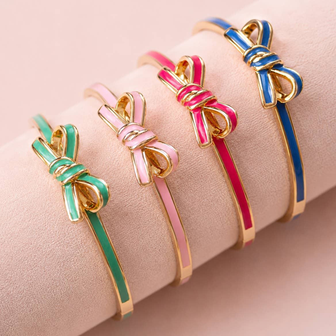 Four colourful enamel bow bangles in mint green, pale pink, bright pink and blue with polished gold detailing