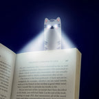 Cat reading light illuminating the pages of an open book in the dark.