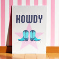 Colourful Howdy A5 art print featuring turquoise cowboy boots over a pink star with bold navy lettering.