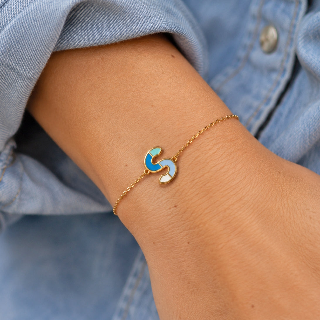 Blue enamel letter S initial bracelet on a delicate gold-tone chain, worn as colourful everyday jewellery.