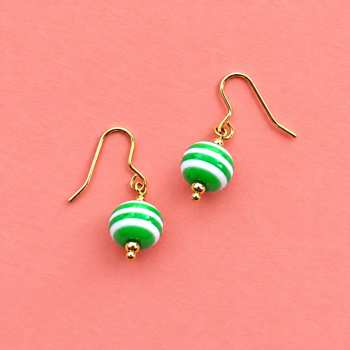 Green and white striped acrylic drop earrings with gold tone hooks on a soft coral pink background.